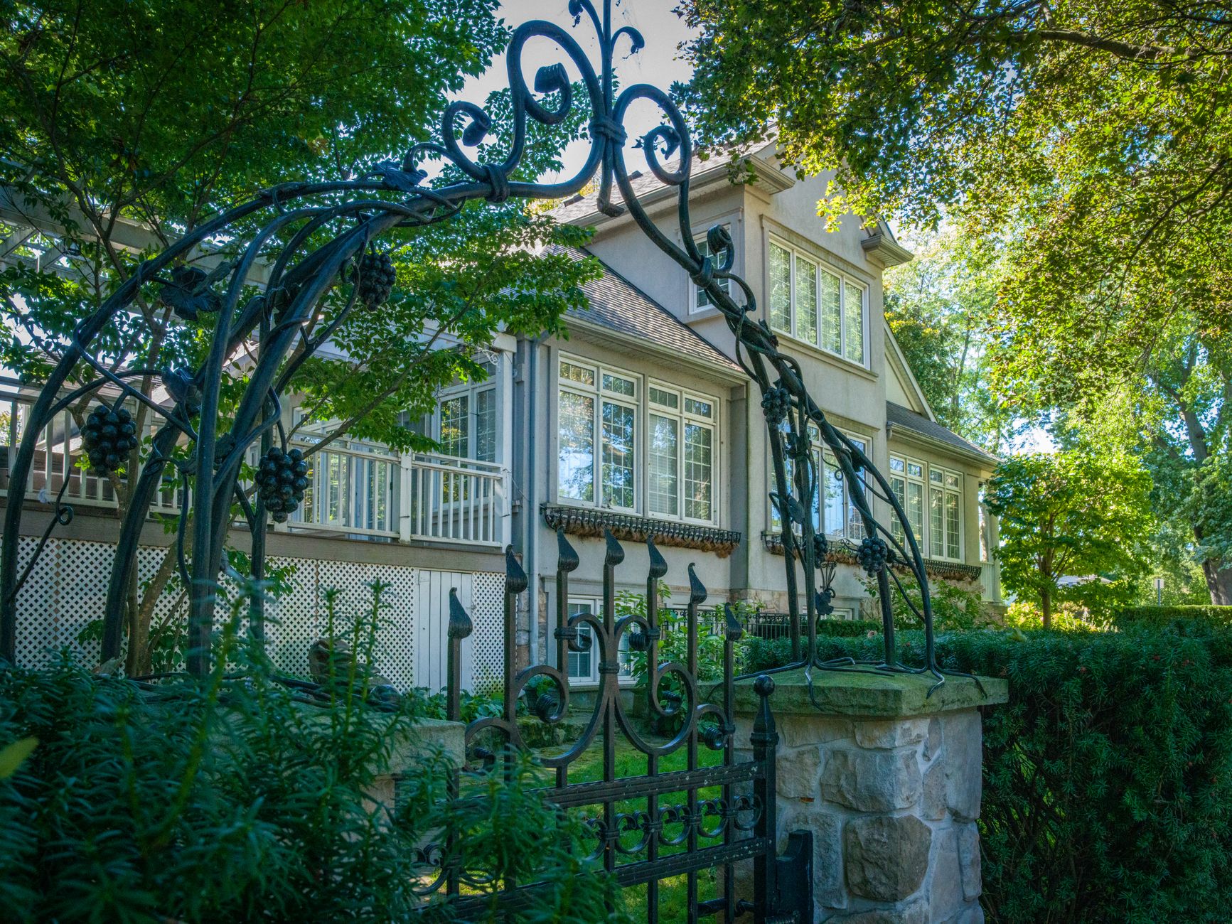 A charming house is visible through a beautifully designed wrought iron gate, surrounded by lush greenery