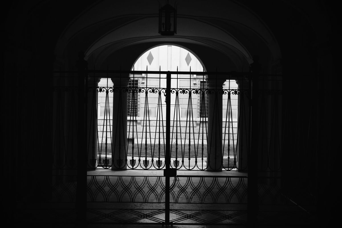 Silhouette of an arched iron gate against a bright sky